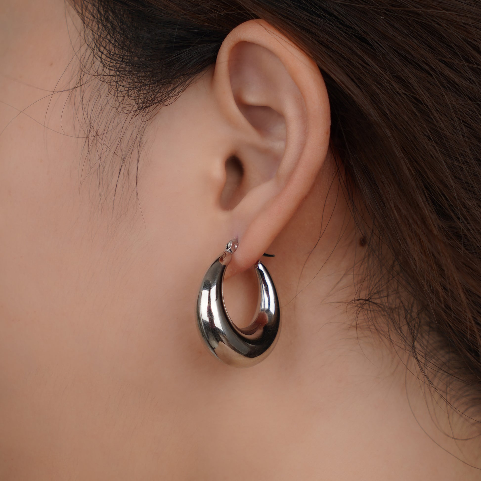 Silver hoop earring worn by a person with a neutral background