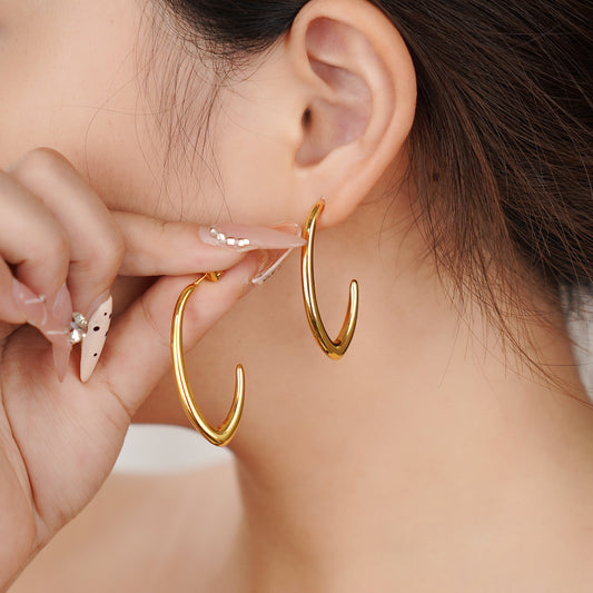 Gold hoop earrings being worn by a person with a blurred background