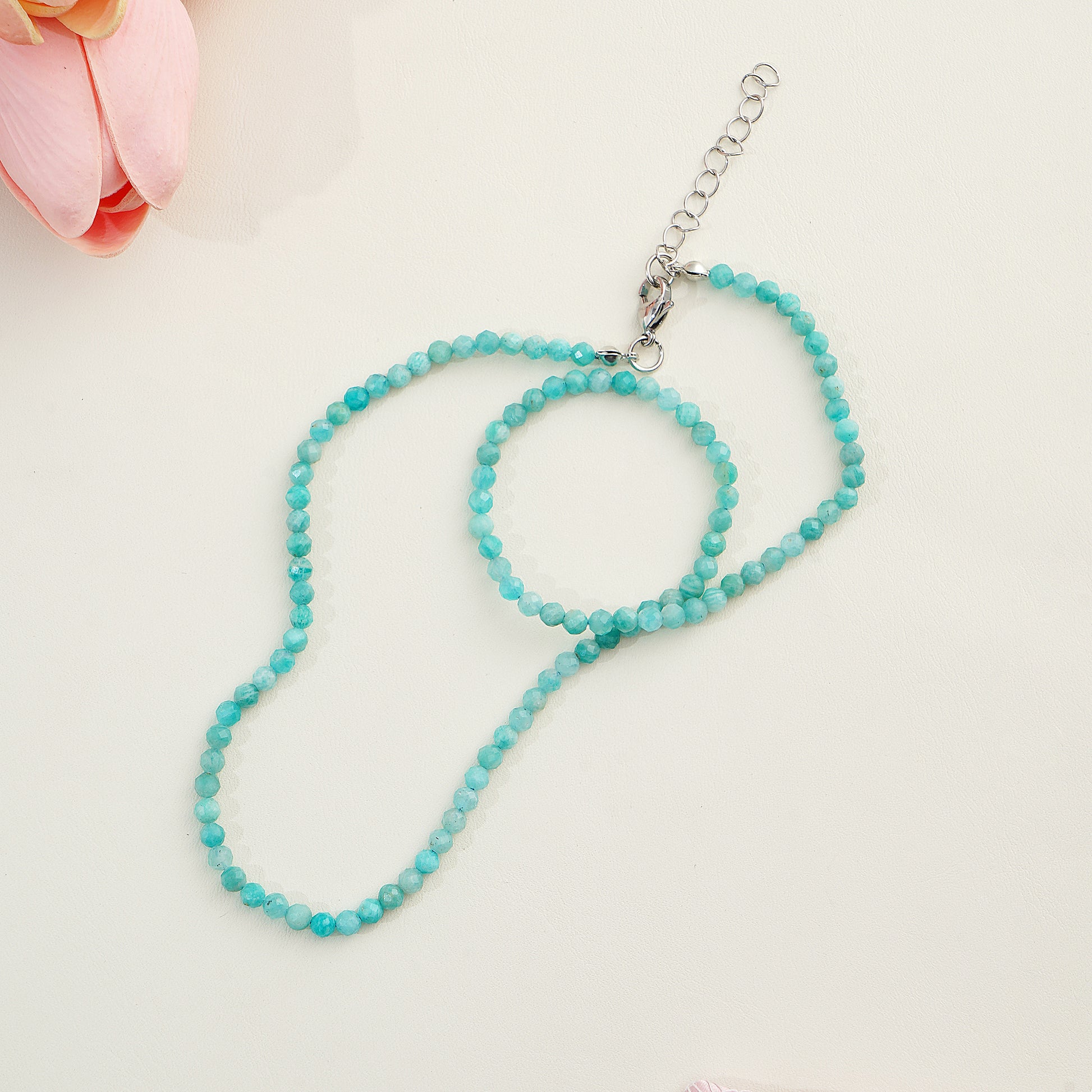 Turquoise beaded necklace on a light pink background with a pink flower.