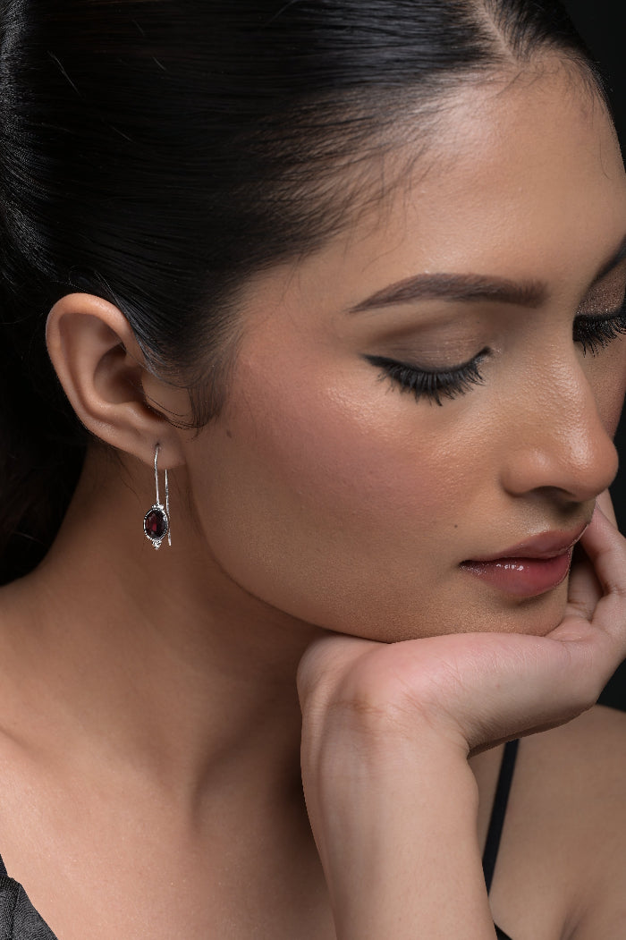 Close-up of a woman wearing a silver earring with a Red Garnet gemstone.