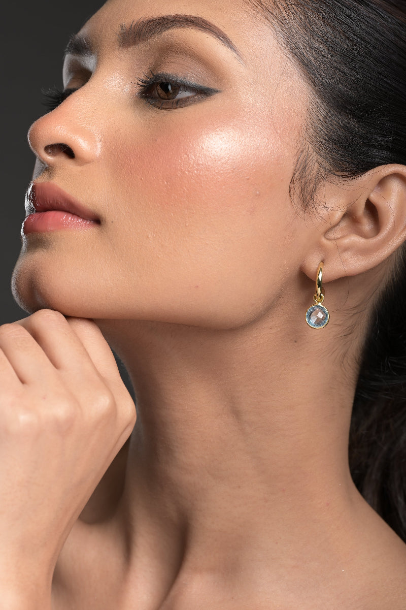 Close-up of a woman wearing a gold earring with a Blue Topaz gemstone on a dark background