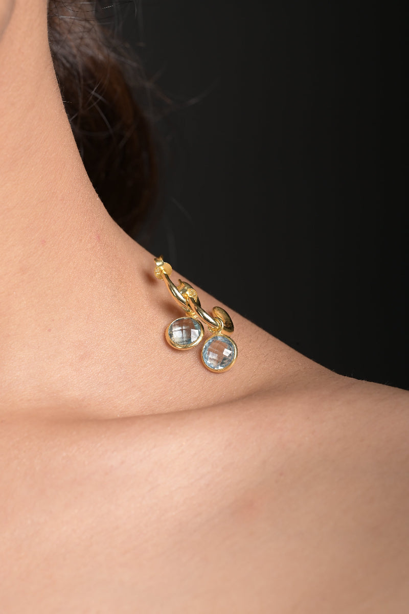 Gold earring with Blue Topaz gemstones worn by a person against a black background
