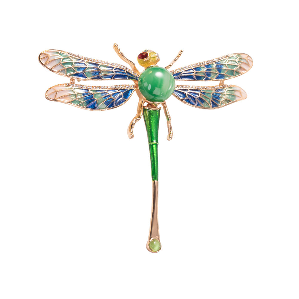 A colorful enameled dragonfly brooch with a green body and blue wings, accented with a red stone.