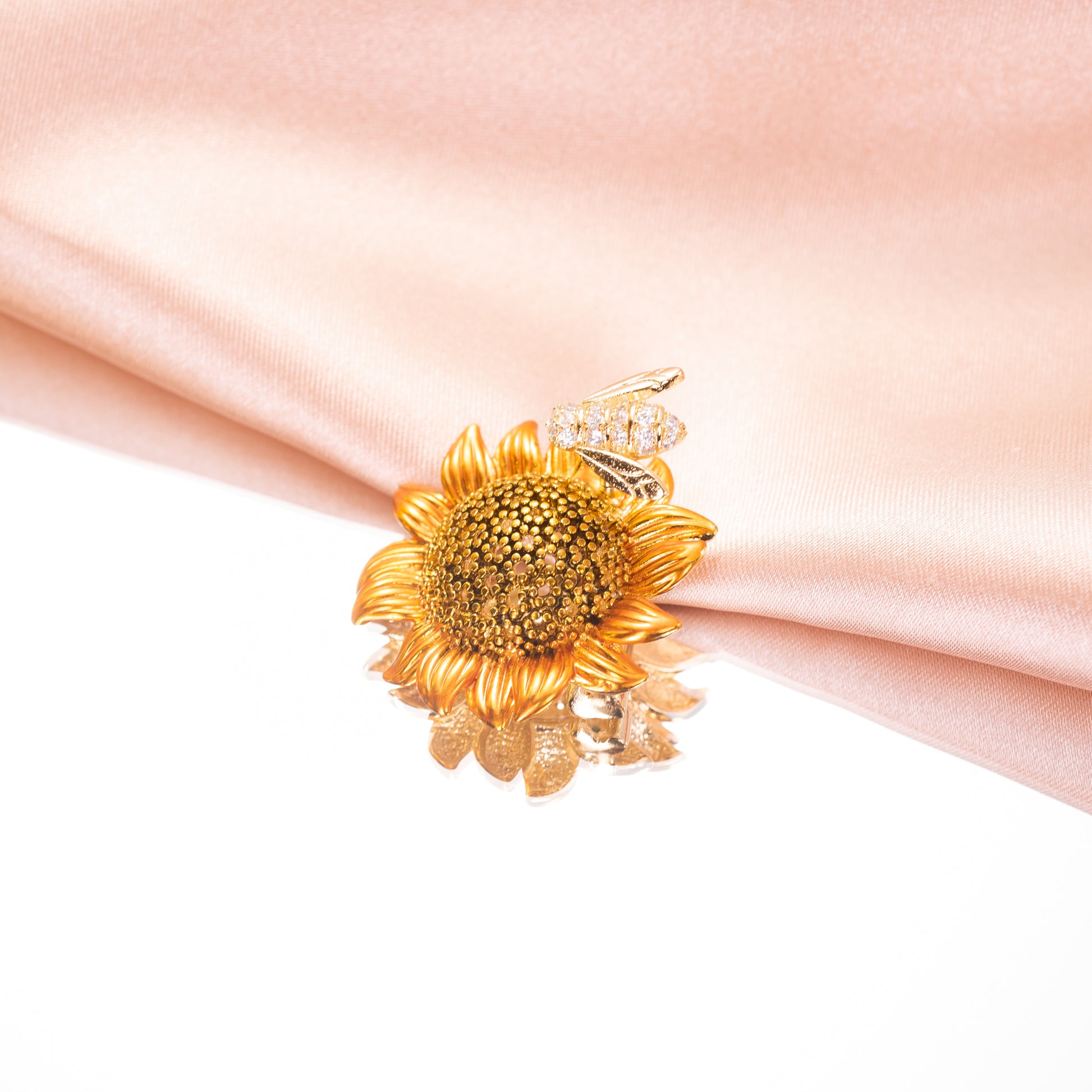 A brooch pin featuring a sunflower with a bee on top, made with cubic zirconia.