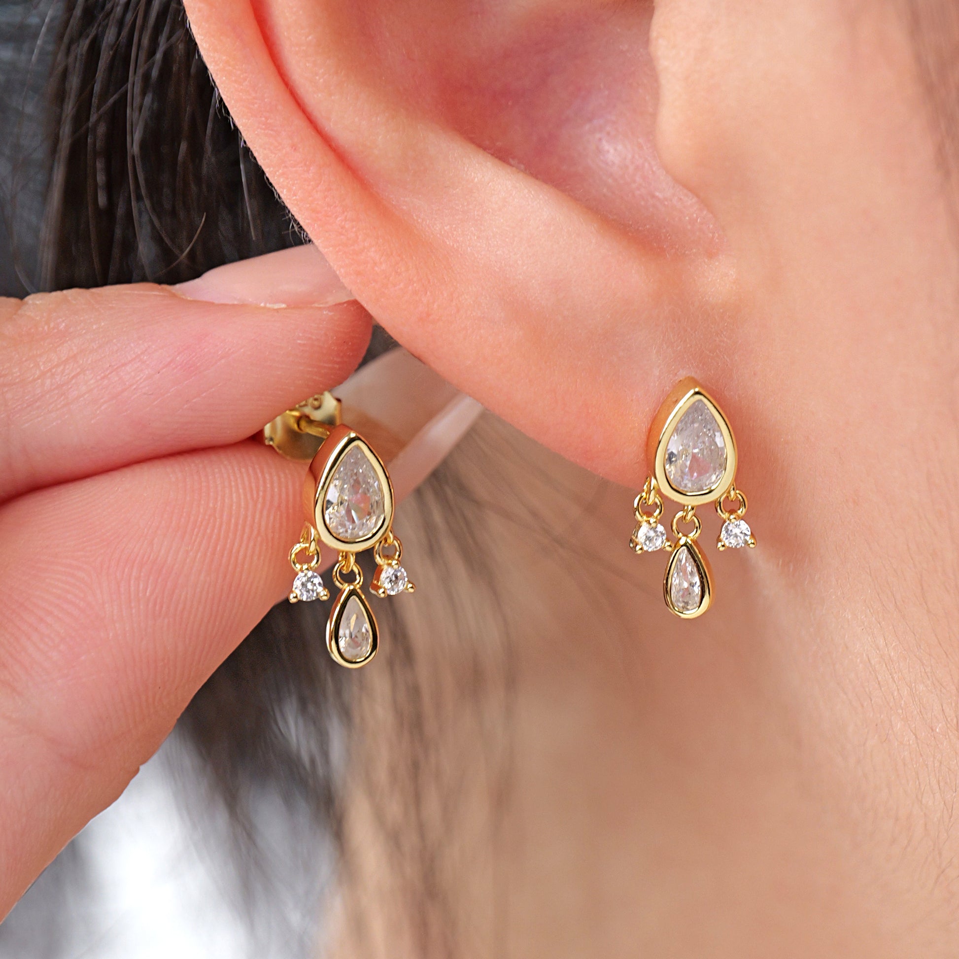 A pair of elegant dangle earrings with pear-shaped clear cubic zirconia stones set in gold-tone mountings.