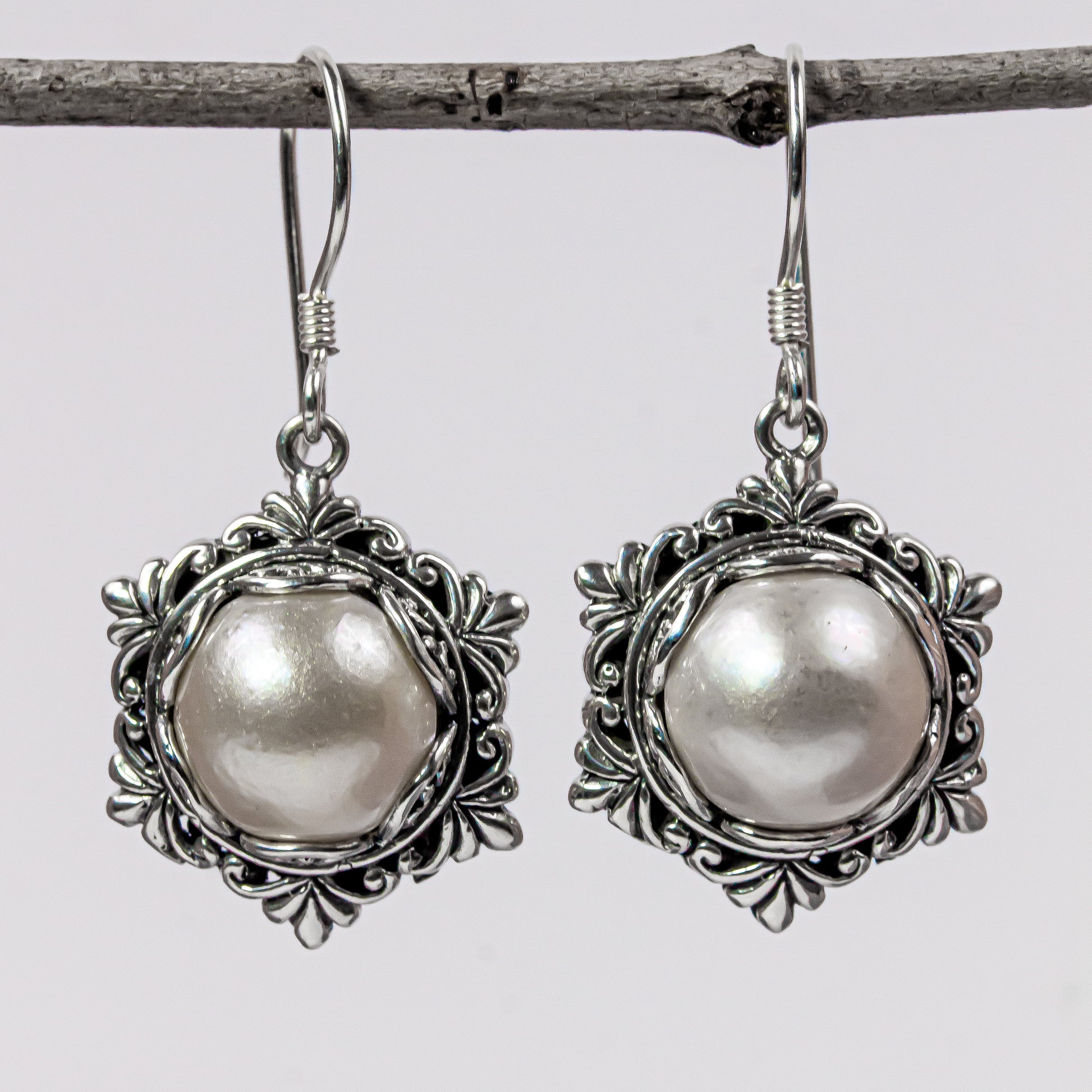 A pair of handcrafted earrings made with natural white mabe pearls and silver accents