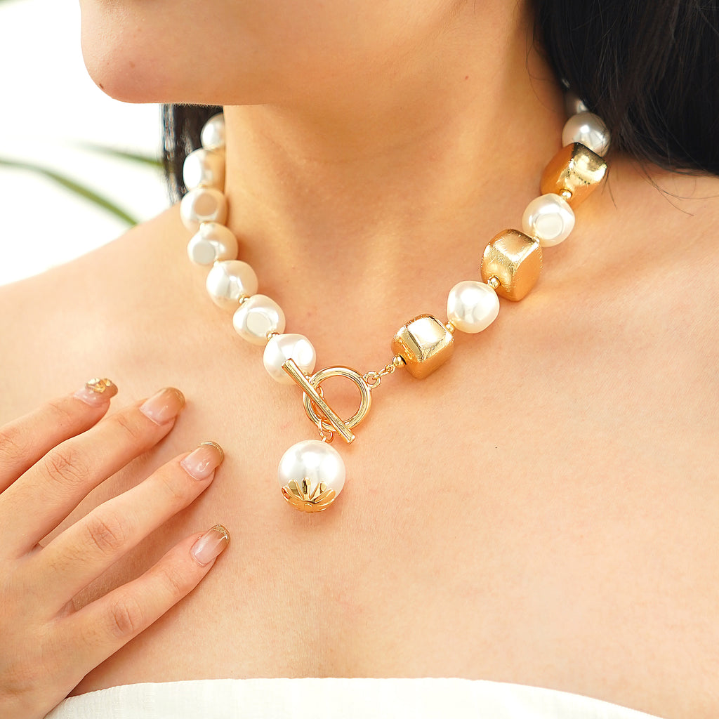 A person wearing a statement pearl necklace with a gold T-lock closure.