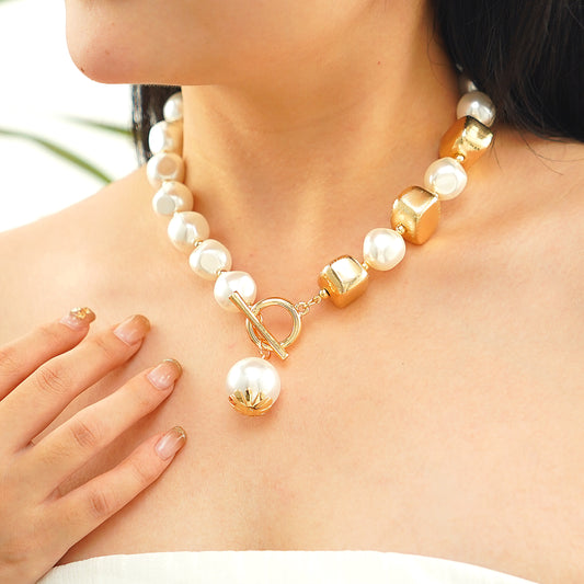 A person wearing a statement pearl necklace with a gold T-lock closure.