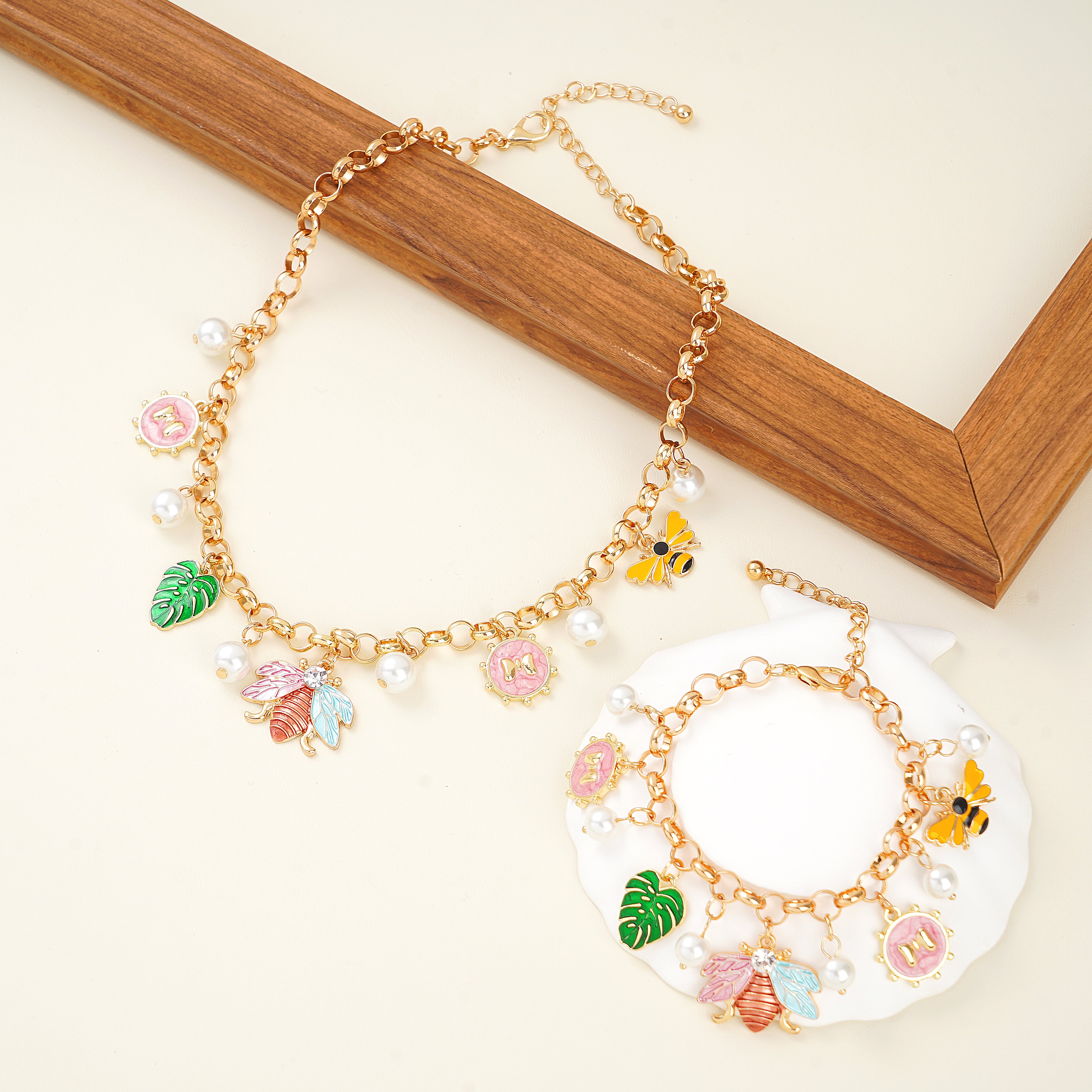 A yellow gold plated charm necklace and bracelet set with nature-inspired designs including charms such as a bee, butterfly, leaves, flowers, and pearls.