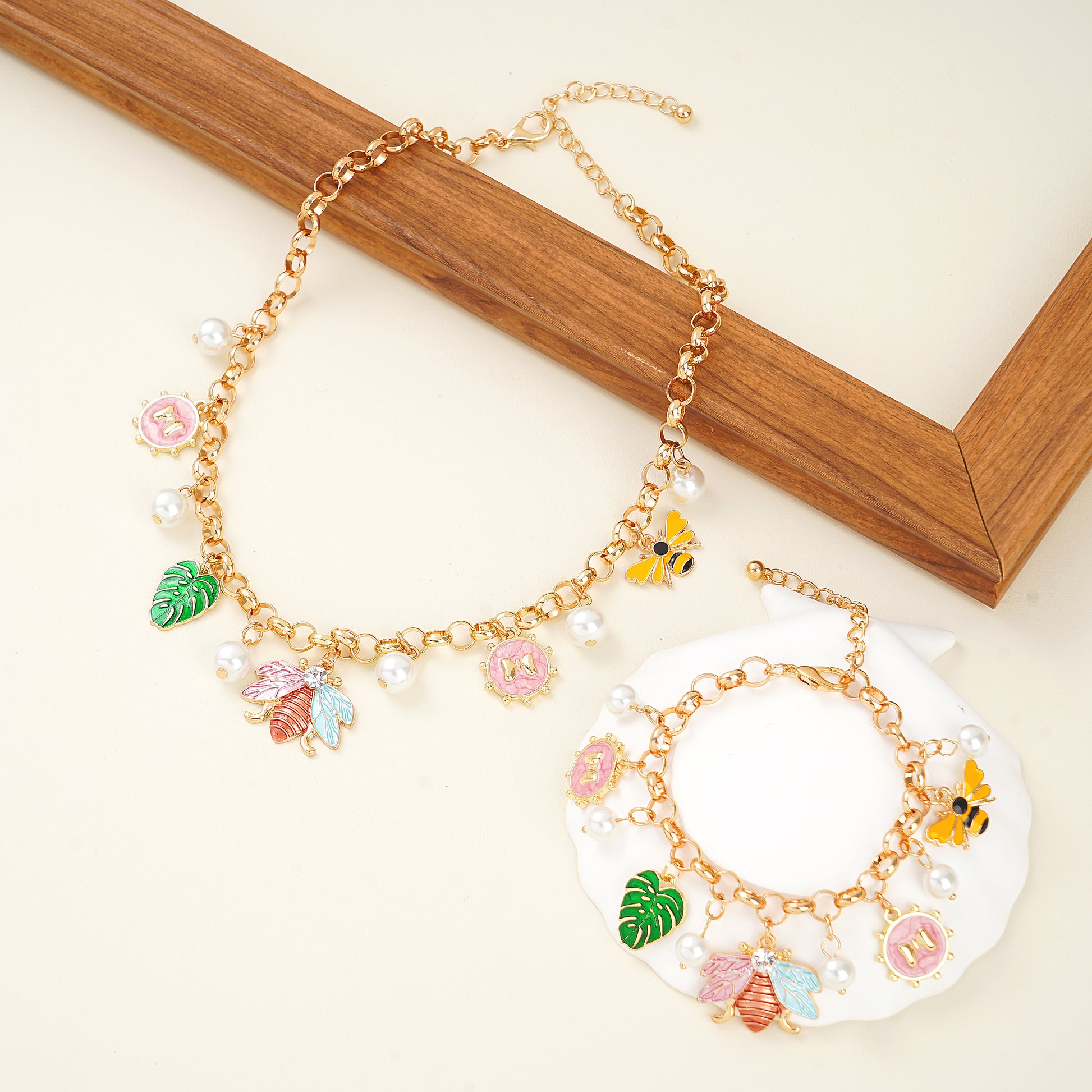 A yellow gold plated charm necklace and bracelet set with nature-inspired designs including charms such as a bee, butterfly, leaves, flowers, and pearls.