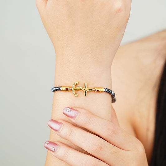 Gold anchor bracelet on a wrist with a neutral background