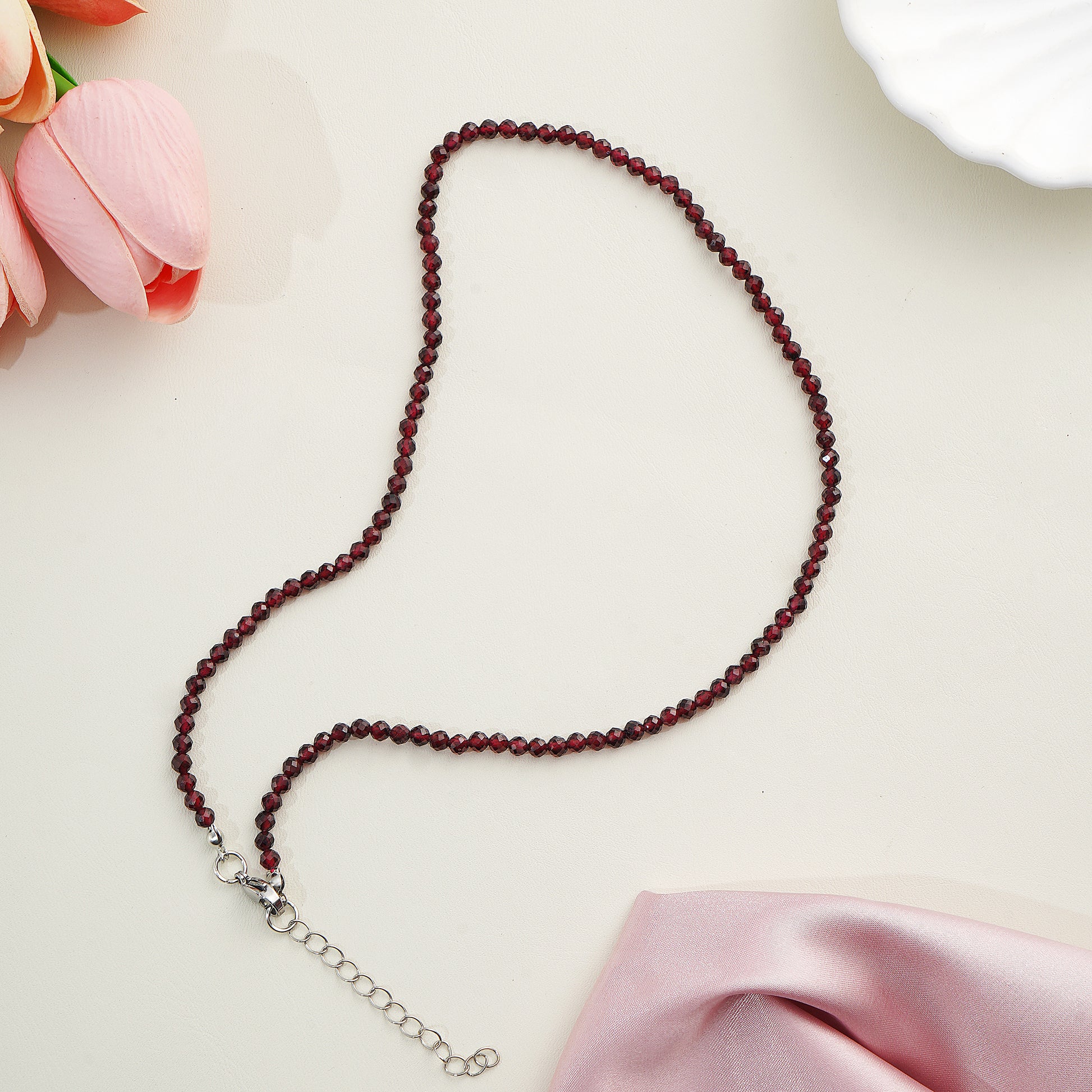 Beaded necklace on a light surface with pink fabric and flowers