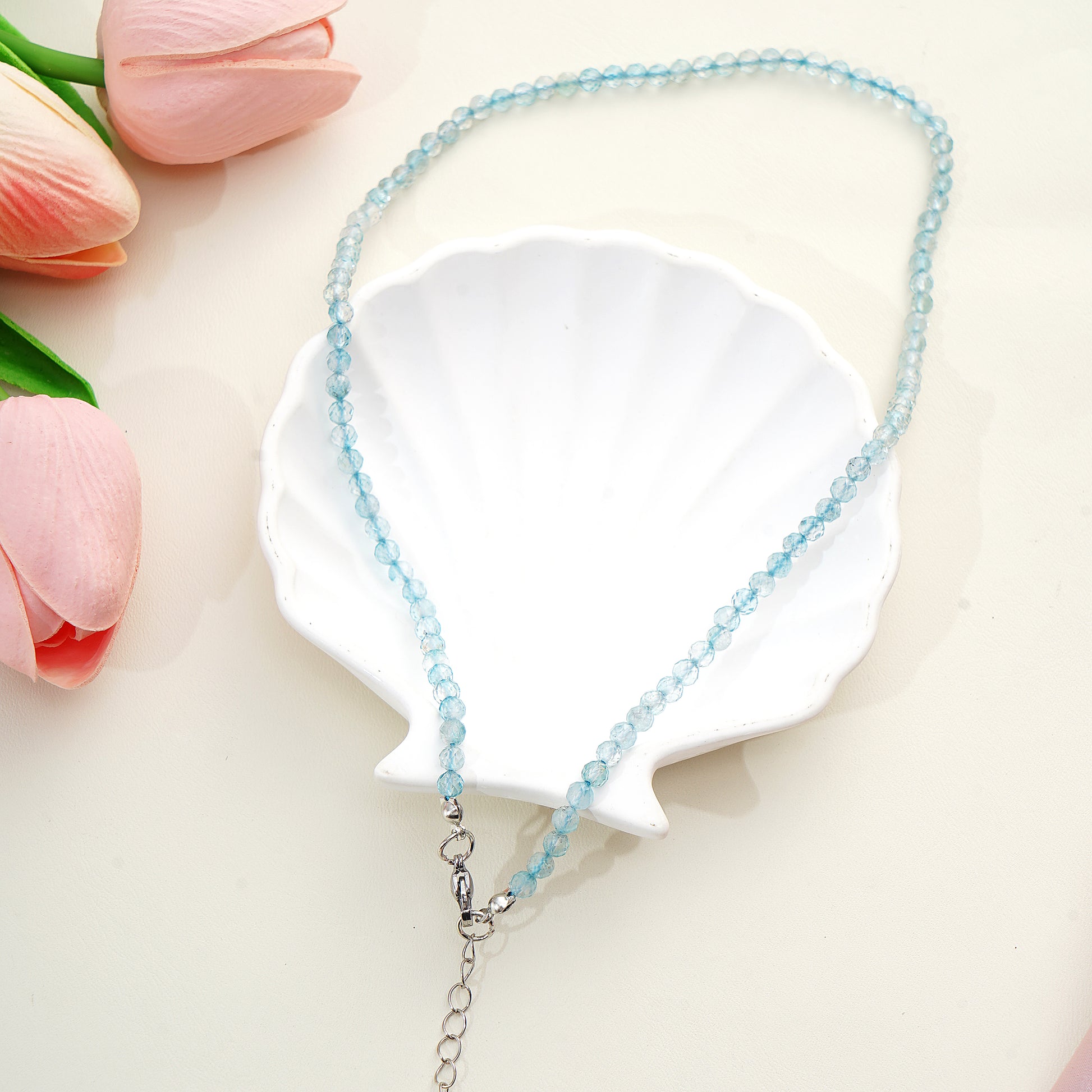 Blue beaded necklace on a white shell with pink tulips in the background