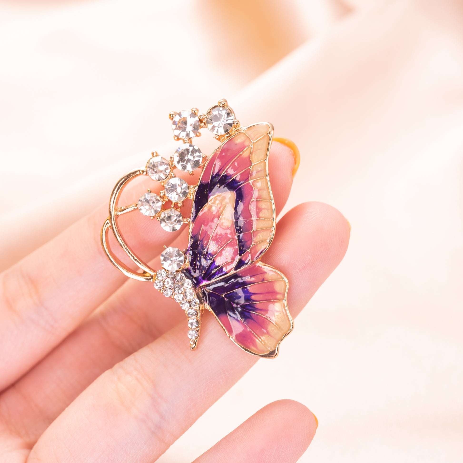 Butterfly-shaped brooch with gemstones held in a hand against a soft background