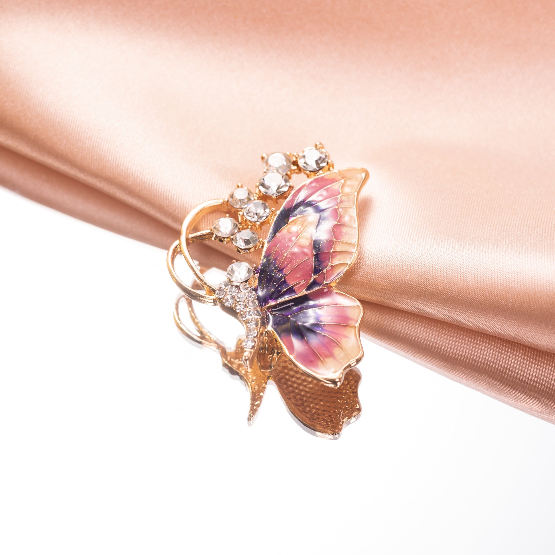 Butterfly-shaped brooch with gemstones on a pink fabric background