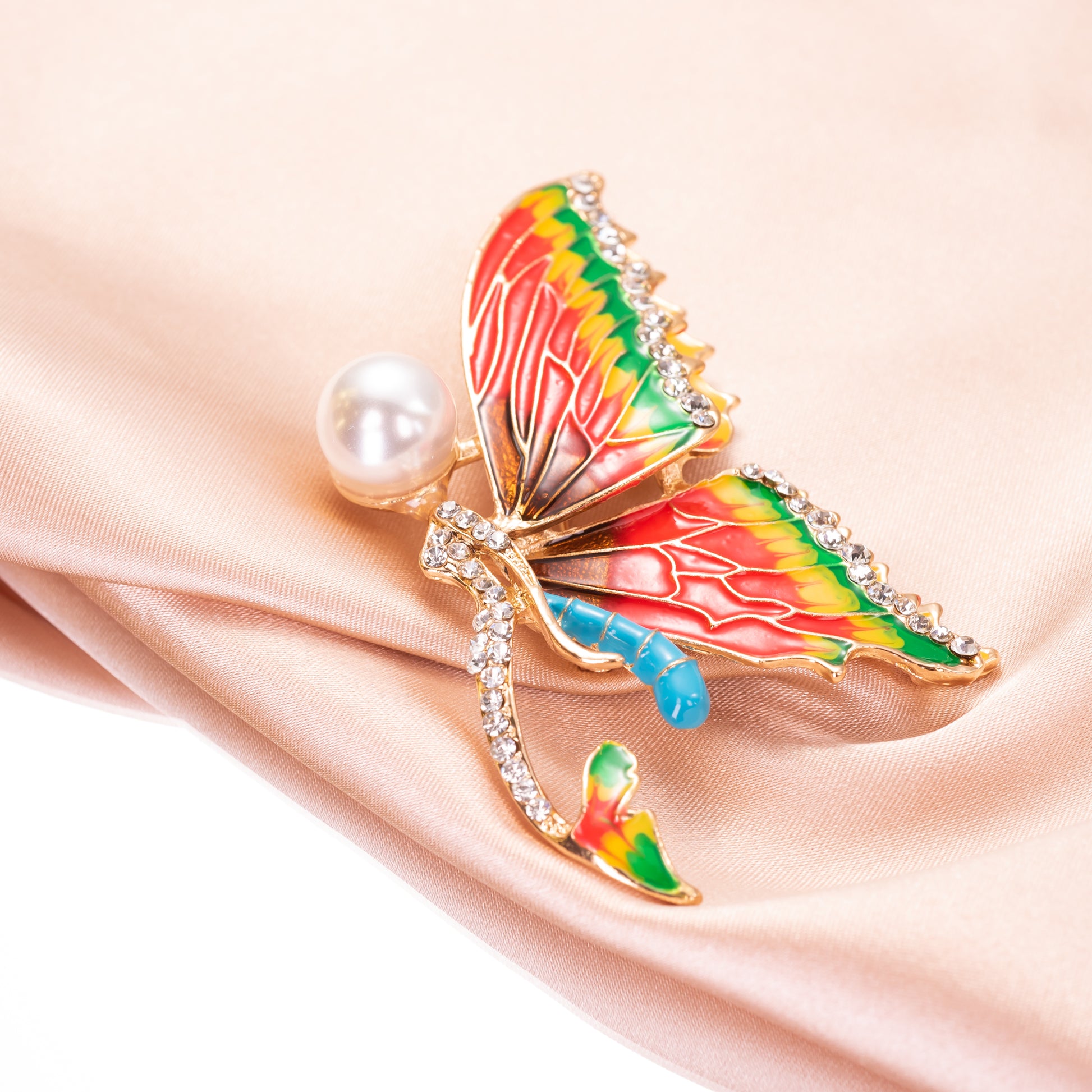 Colorful butterfly-shaped brooch with a pearl on a beige fabric background