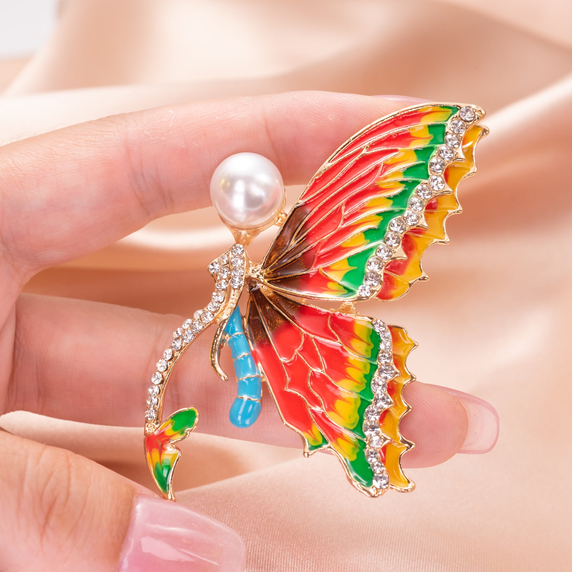 Colorful butterfly-shaped brooch with pearl and gemstones held in a hand.