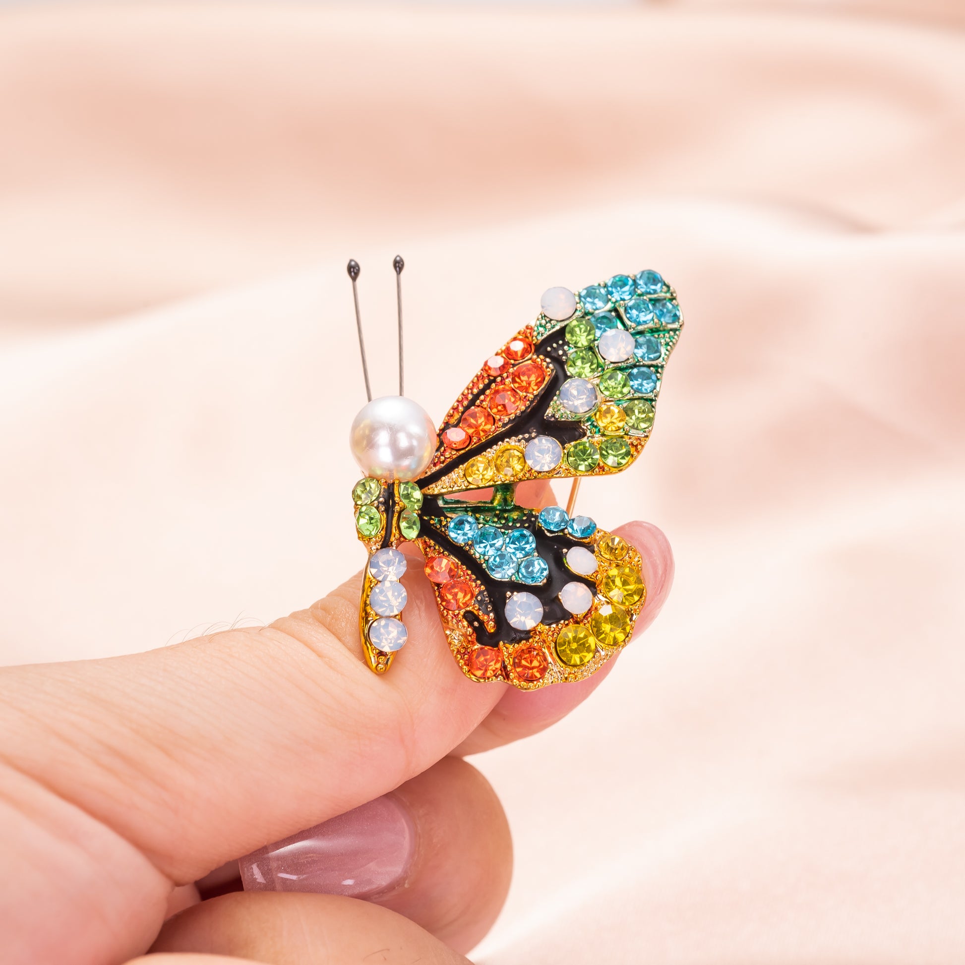 Colorful butterfly brooch with gemstones held between fingers against a soft pink background