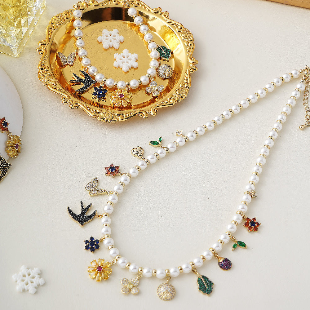 Pearl necklace with charms on a white surface, with a gold tray holding additional jewelry items-Stars and Vogue