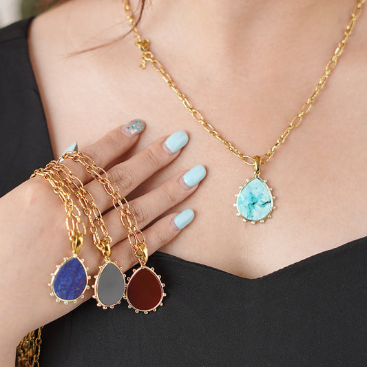 Three gold necklaces with teardrop-shaped Gemstone pendants held in a hand.