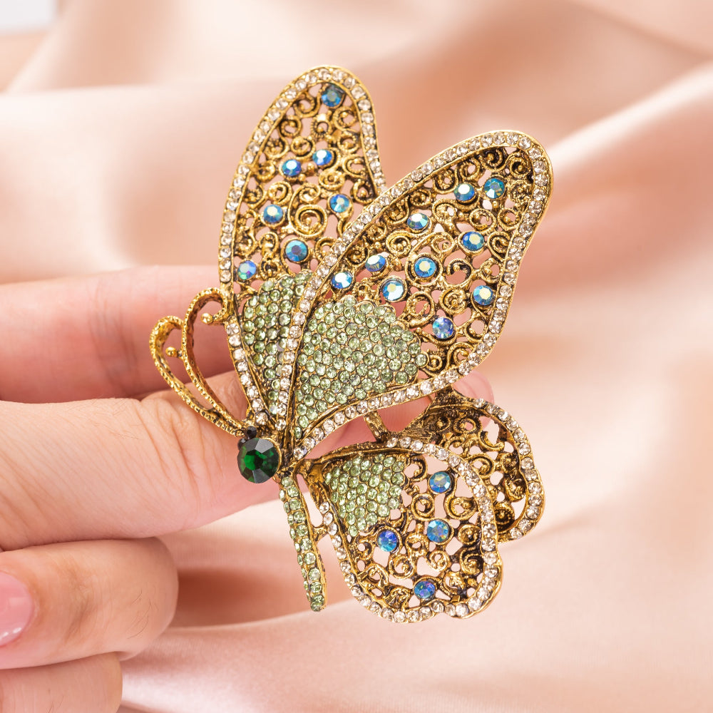 Butterfly-shaped brooch with gold, green, and blue gemstones held in a hand.