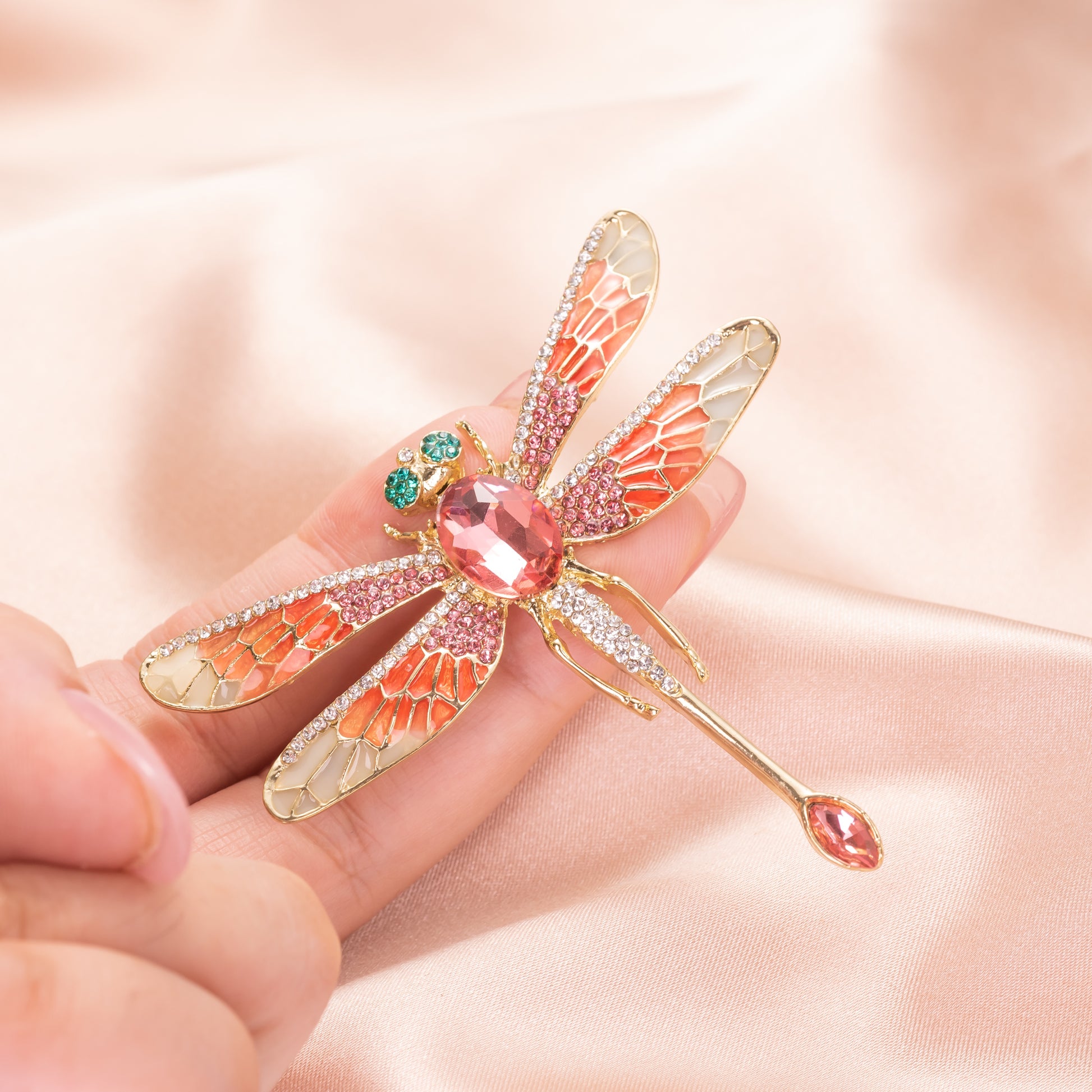 Decorative dragonfly brooch with gemstones held in a hand against a soft pink background
