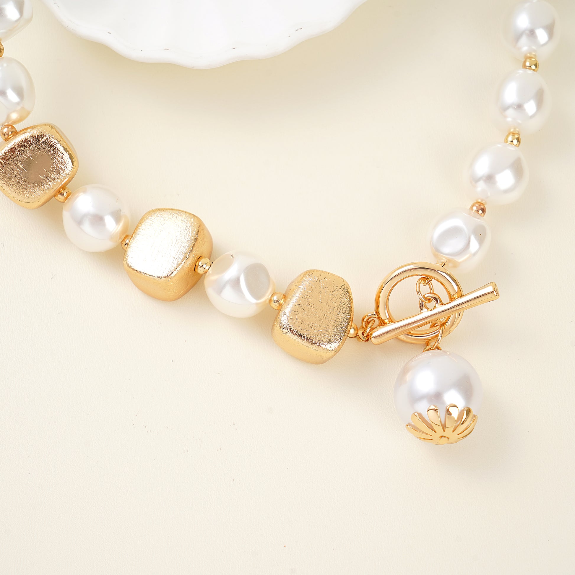 Front view of a statement necklace with oversized white shell pearls and a gold T-lock toggle clasp