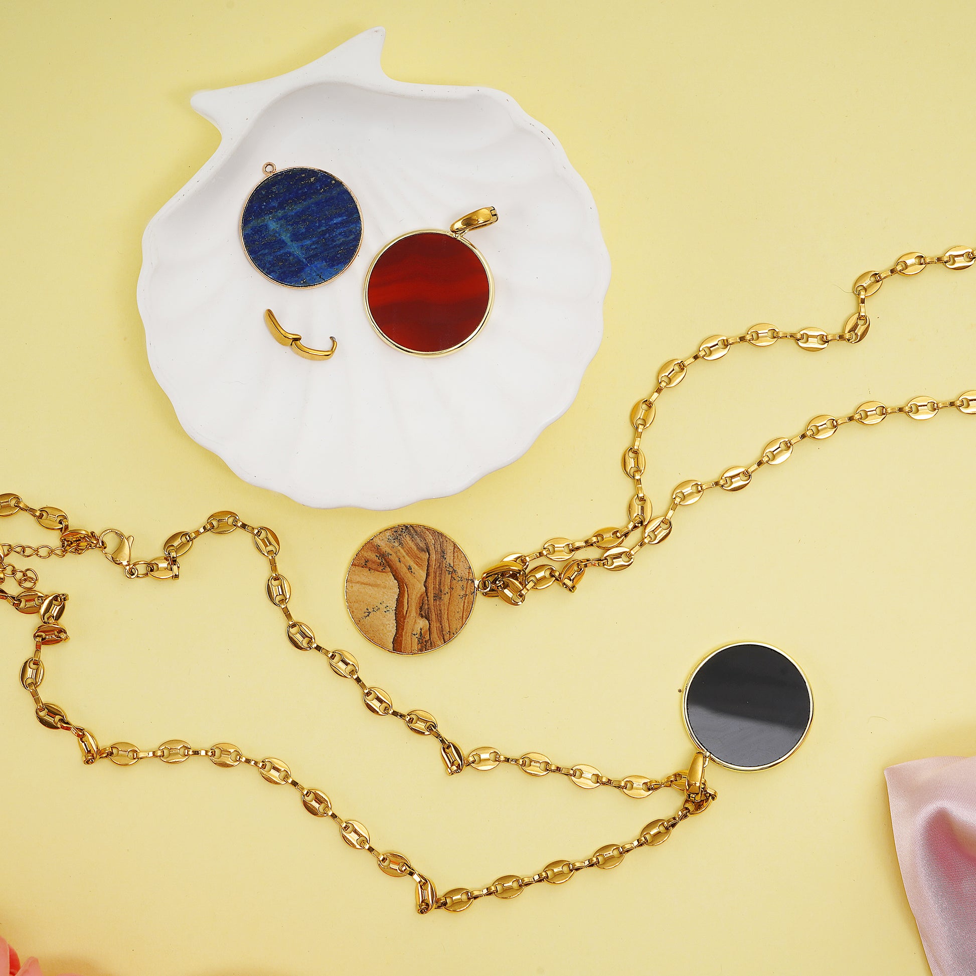 Gold necklaces with round Gemstone pendants on a decorative surface with flowers.