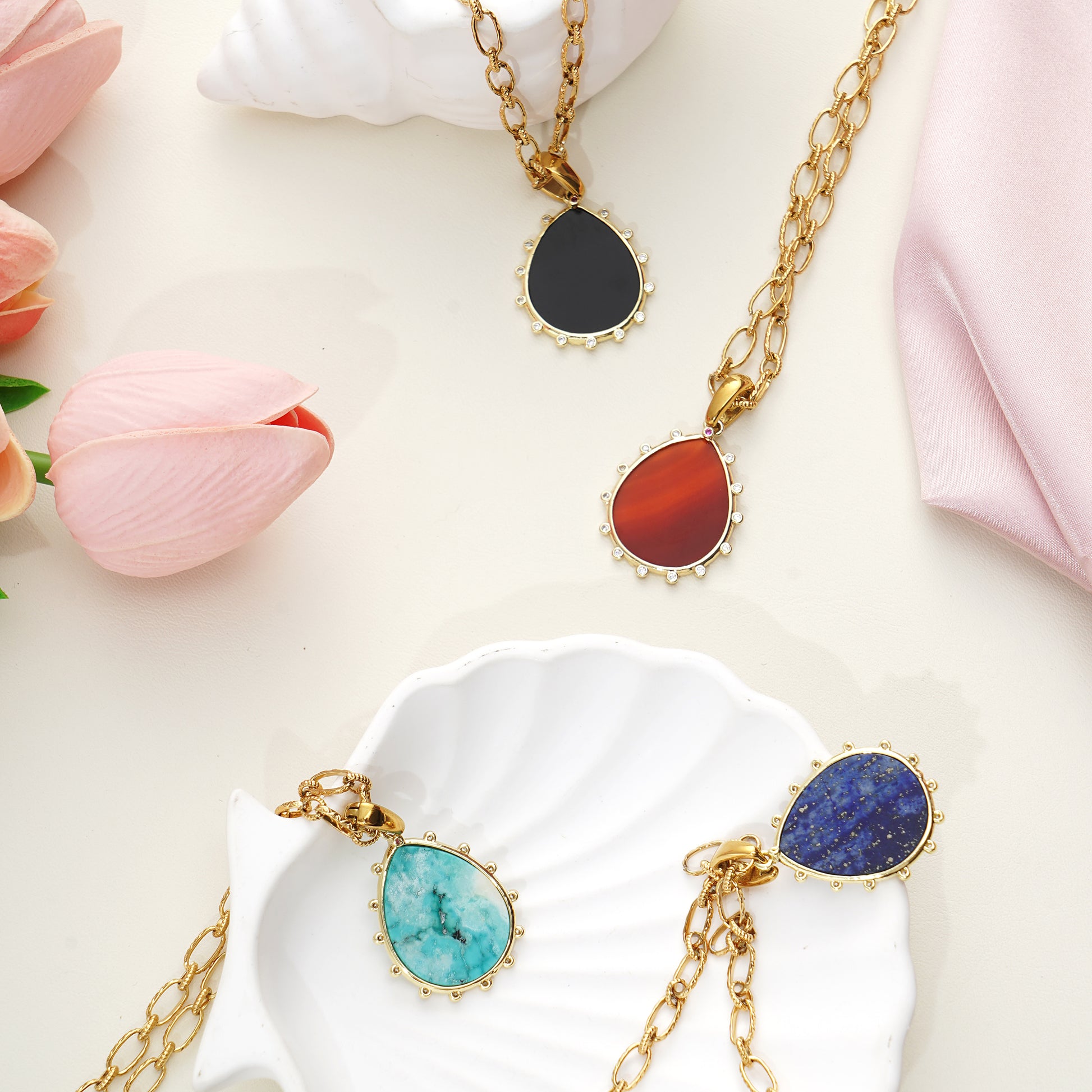 Gold necklaces with colorful Gemstone pendant stones on a white surface with pink flowers.