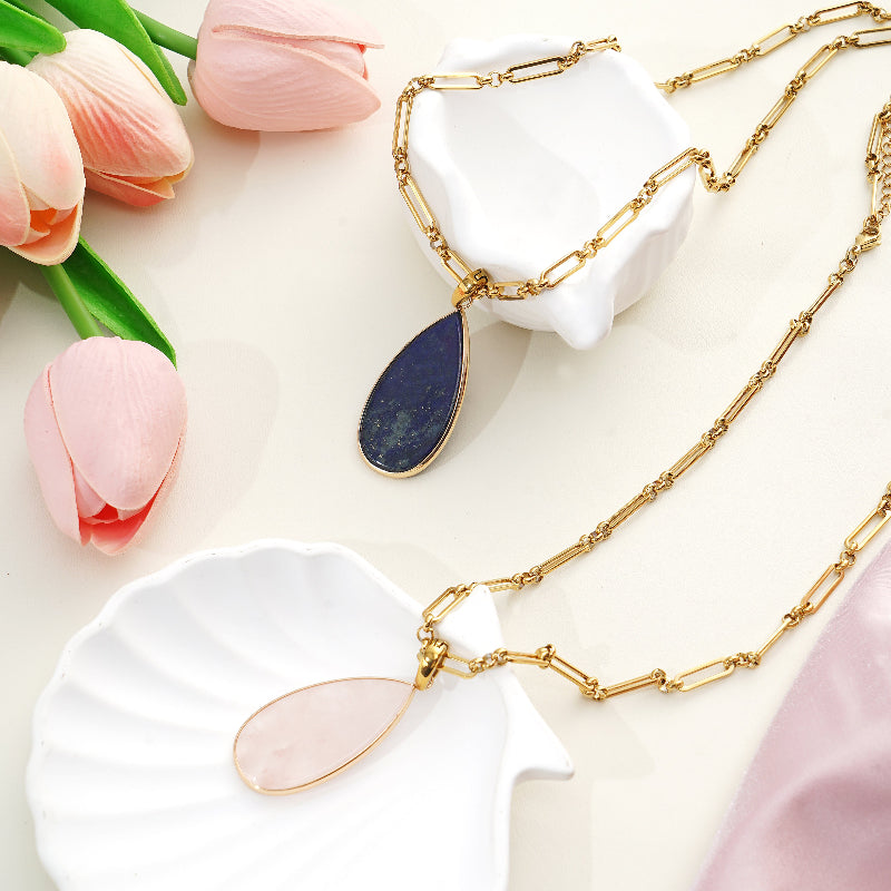 Gold necklaces with teardrop Gemstone pendants on a white surface with pink tulips.