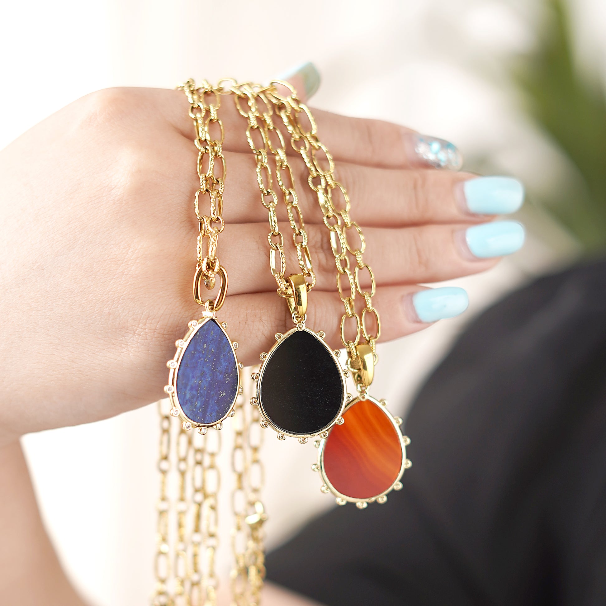 Three gold necklaces with teardrop-shaped Gemstone pendants held in a hand.