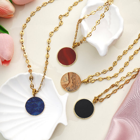 Gold necklaces with round Gemstone pendants on a decorative surface with flowers.