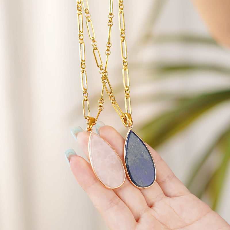 Gold necklaces with teardrop Gemstone pendants held by a hand against a blurred natural background