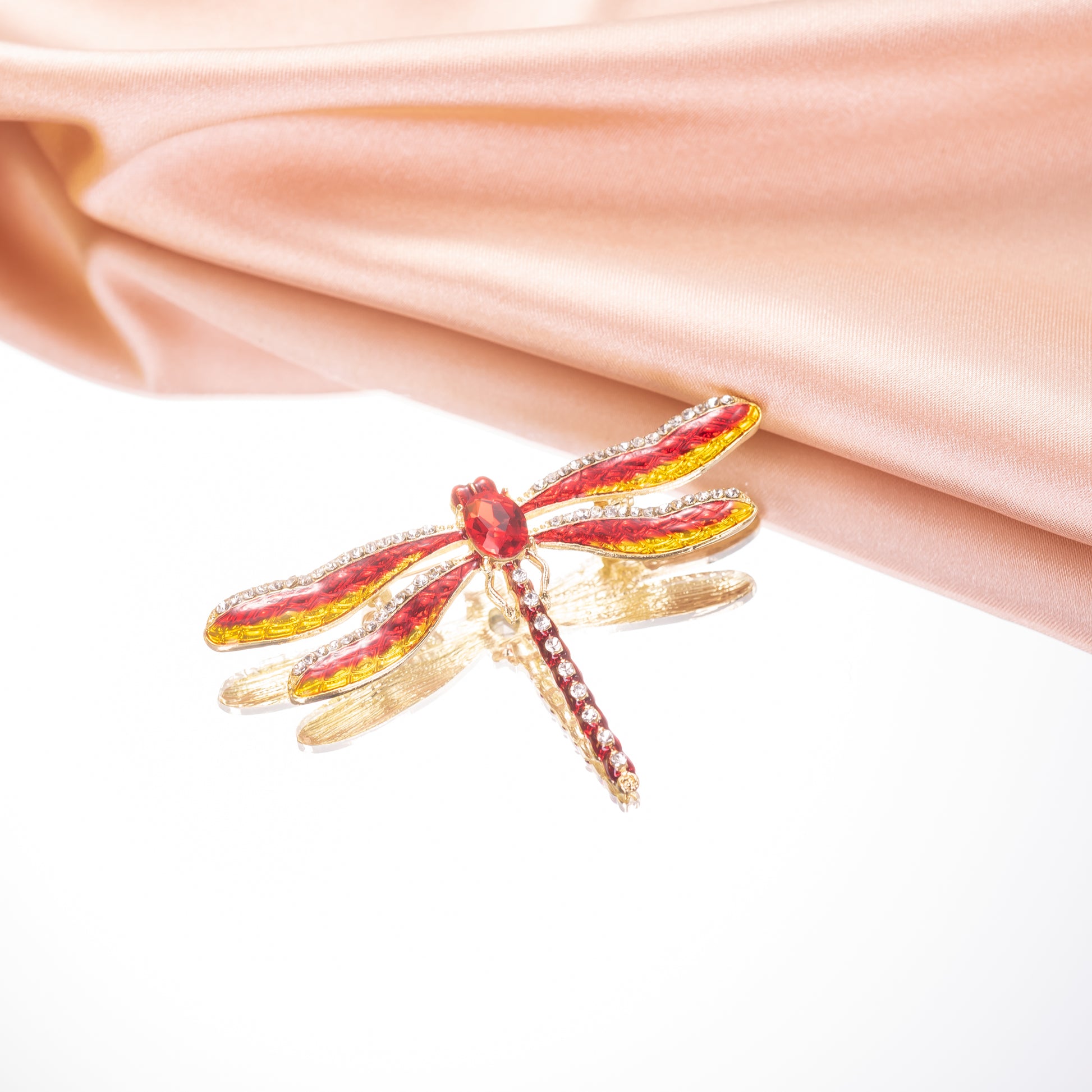 Gold and red dragonfly-shaped brooch on a pink fabric background