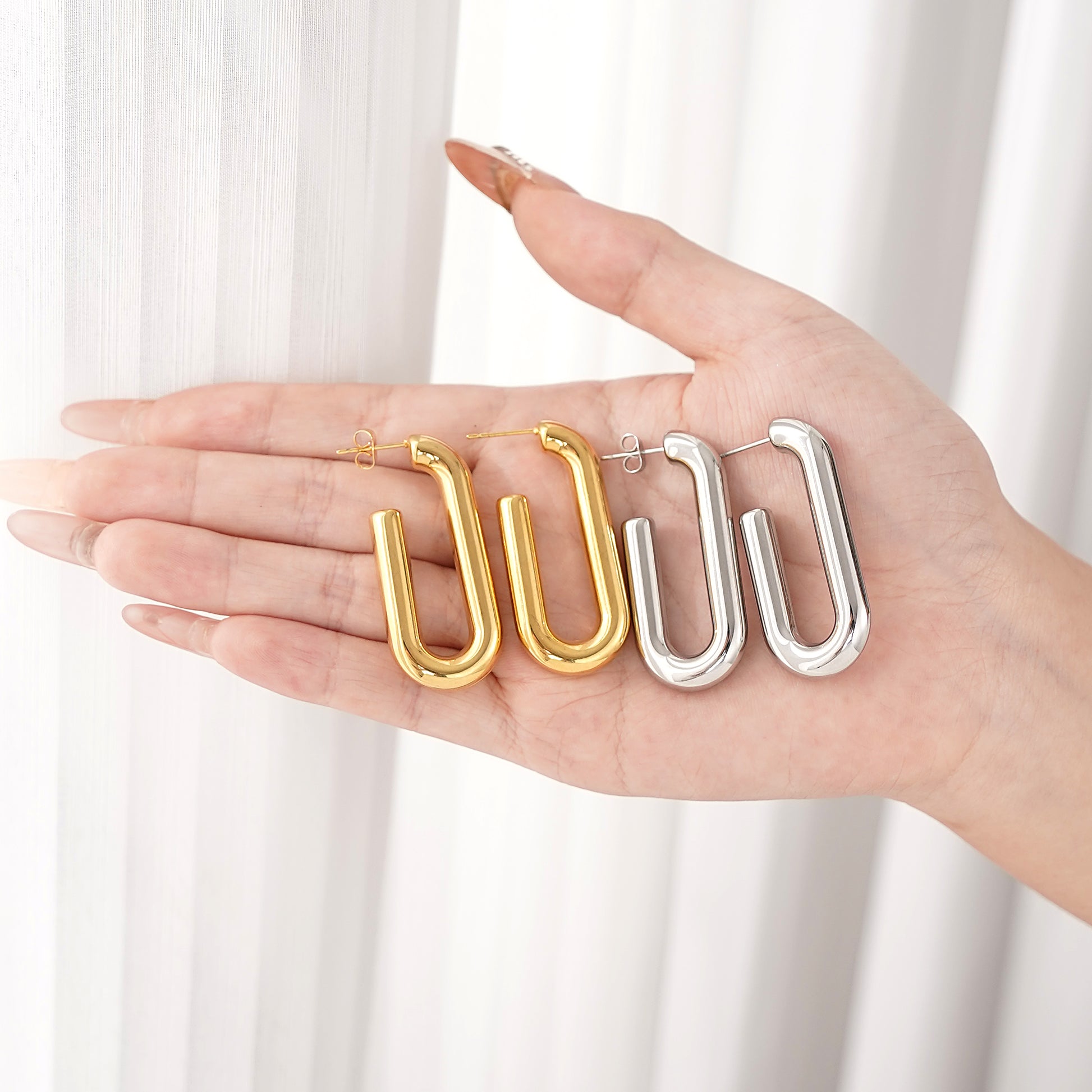 Gold and silver U-shaped earrings held in a hand against a white background
