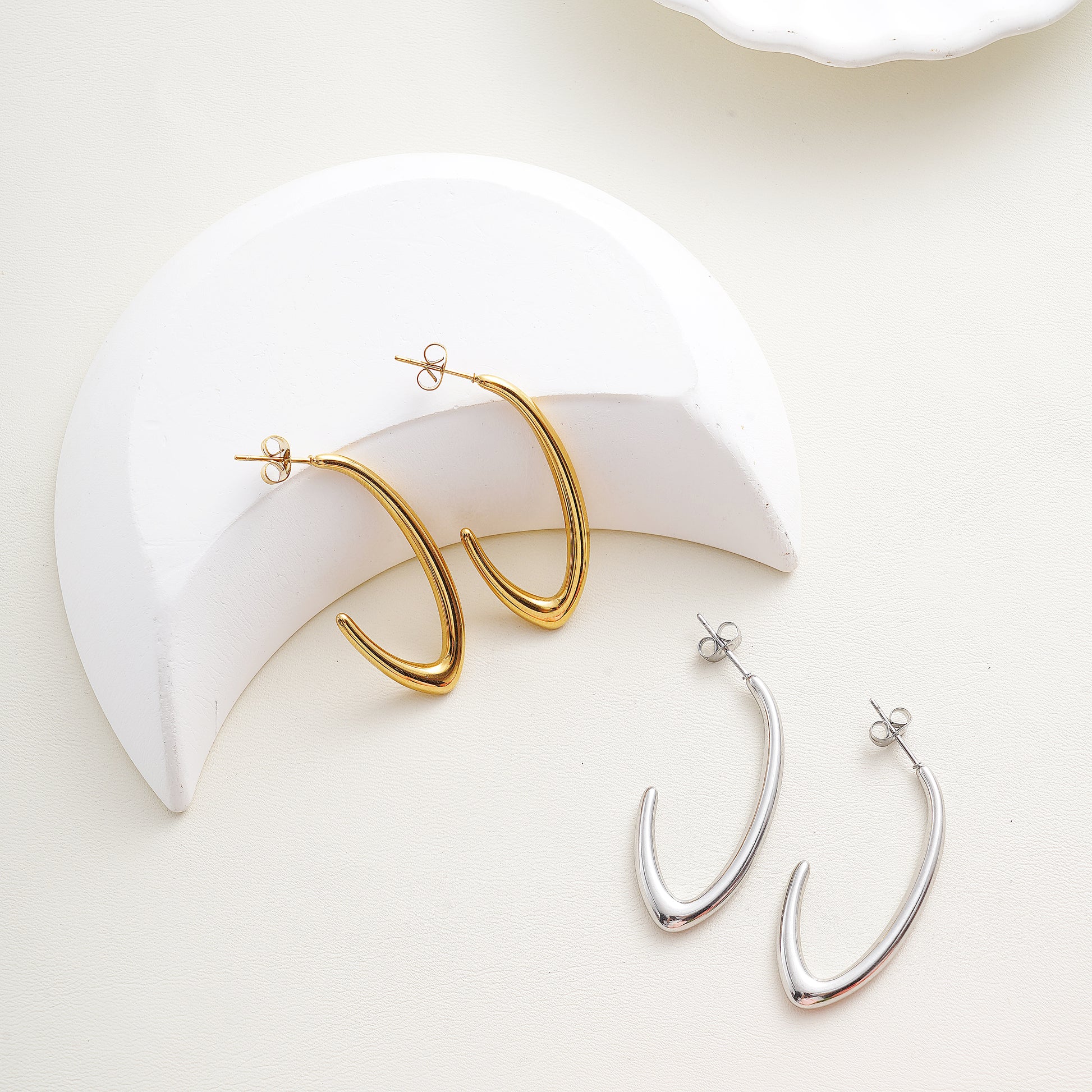 Gold and silver hoop earrings on a white surface with a white crescent moon-shaped object.