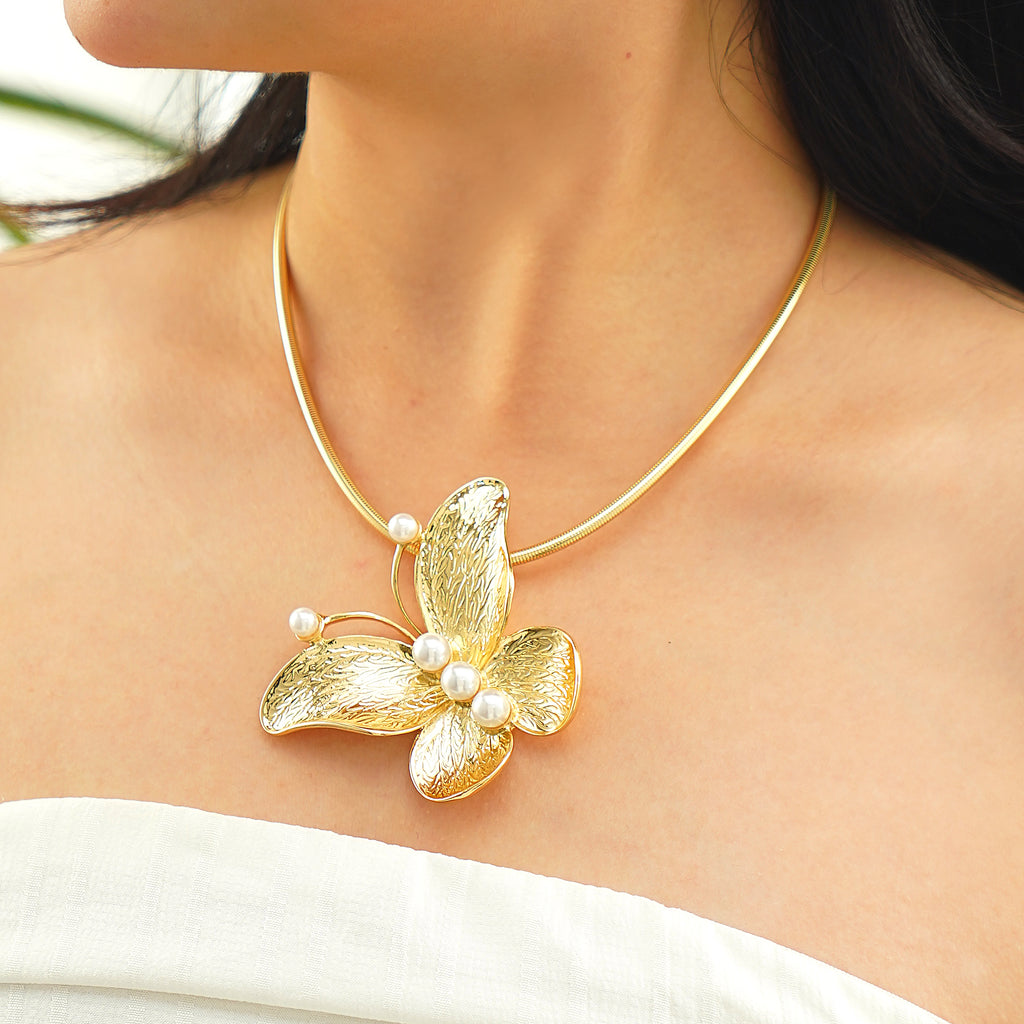 Gold butterfly necklace with pearl details on a person wearing a white top.
