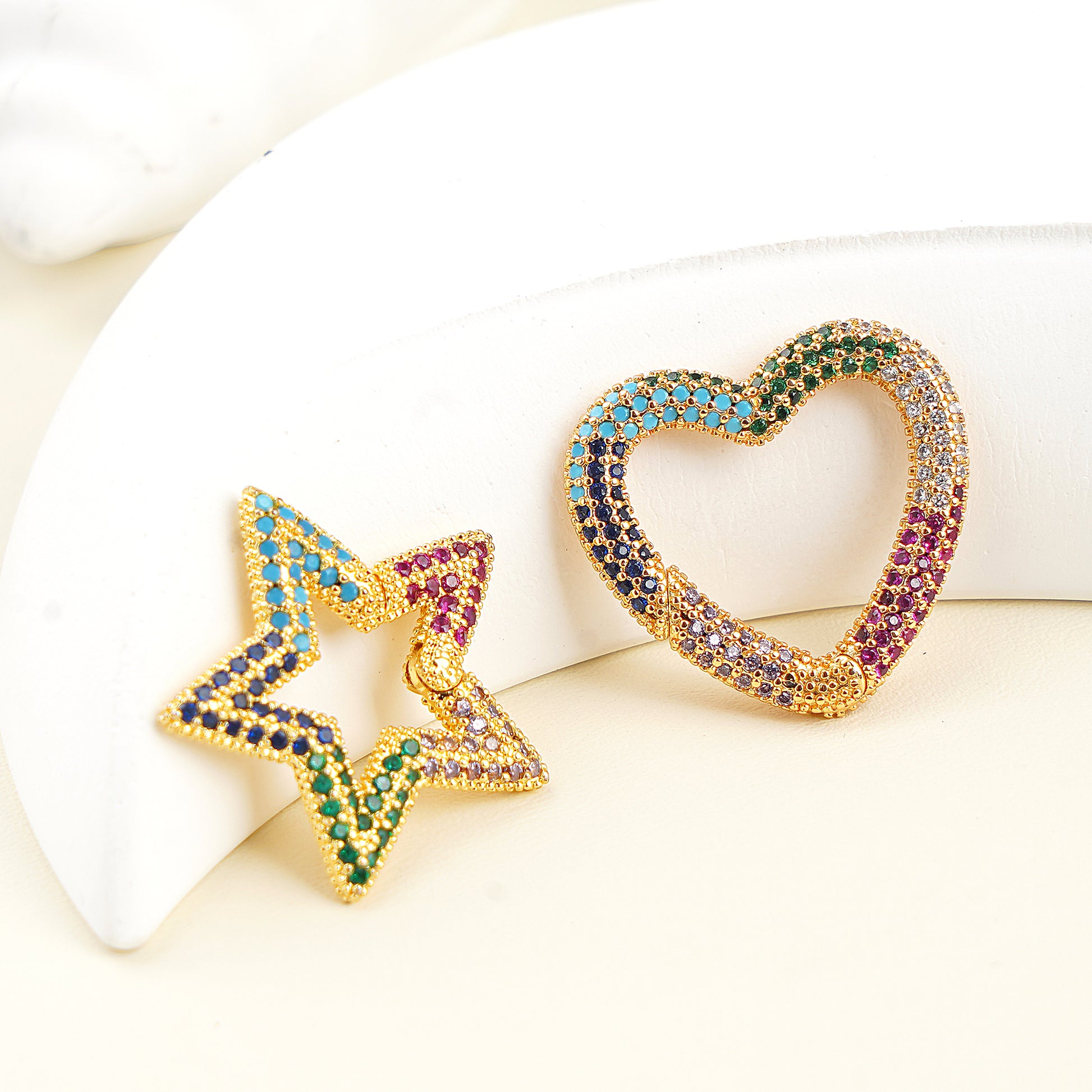 Gold earrings shaped like a star and a heart with gemstones on a white background