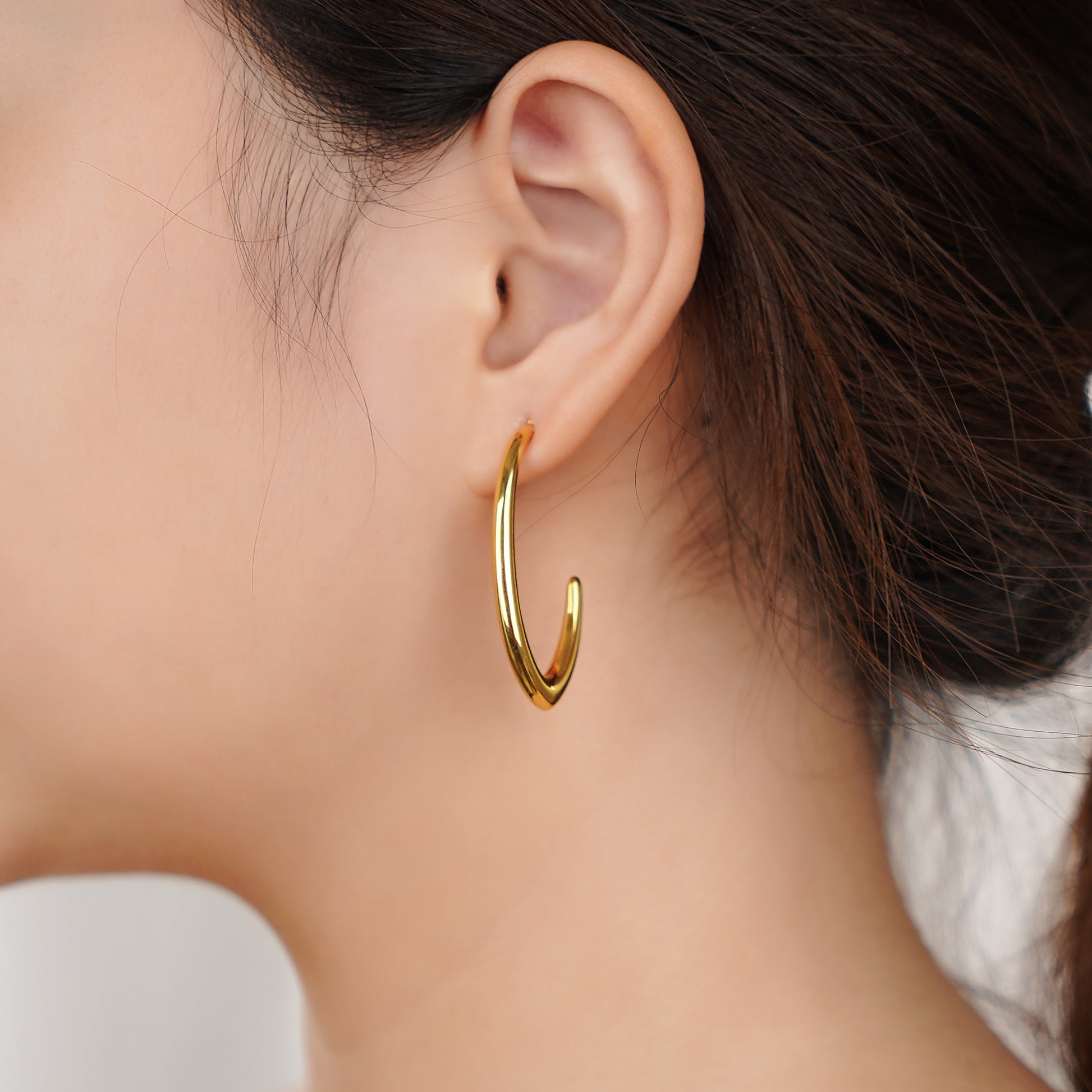 Gold hoop earring worn by a person with a neutral background