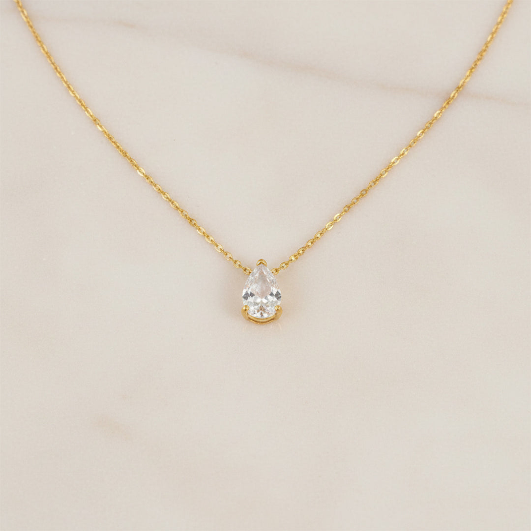 Gold necklace with a teardrop-shaped diamond pendant on a beige background