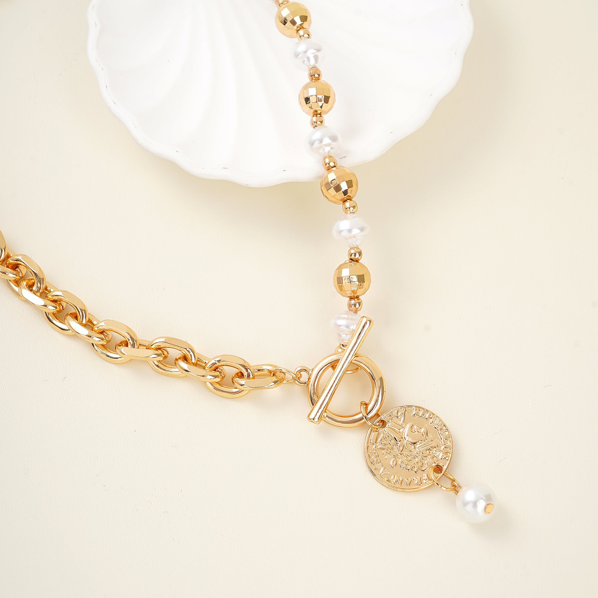 Gold necklace with beads and a toggle clasp on a beige background