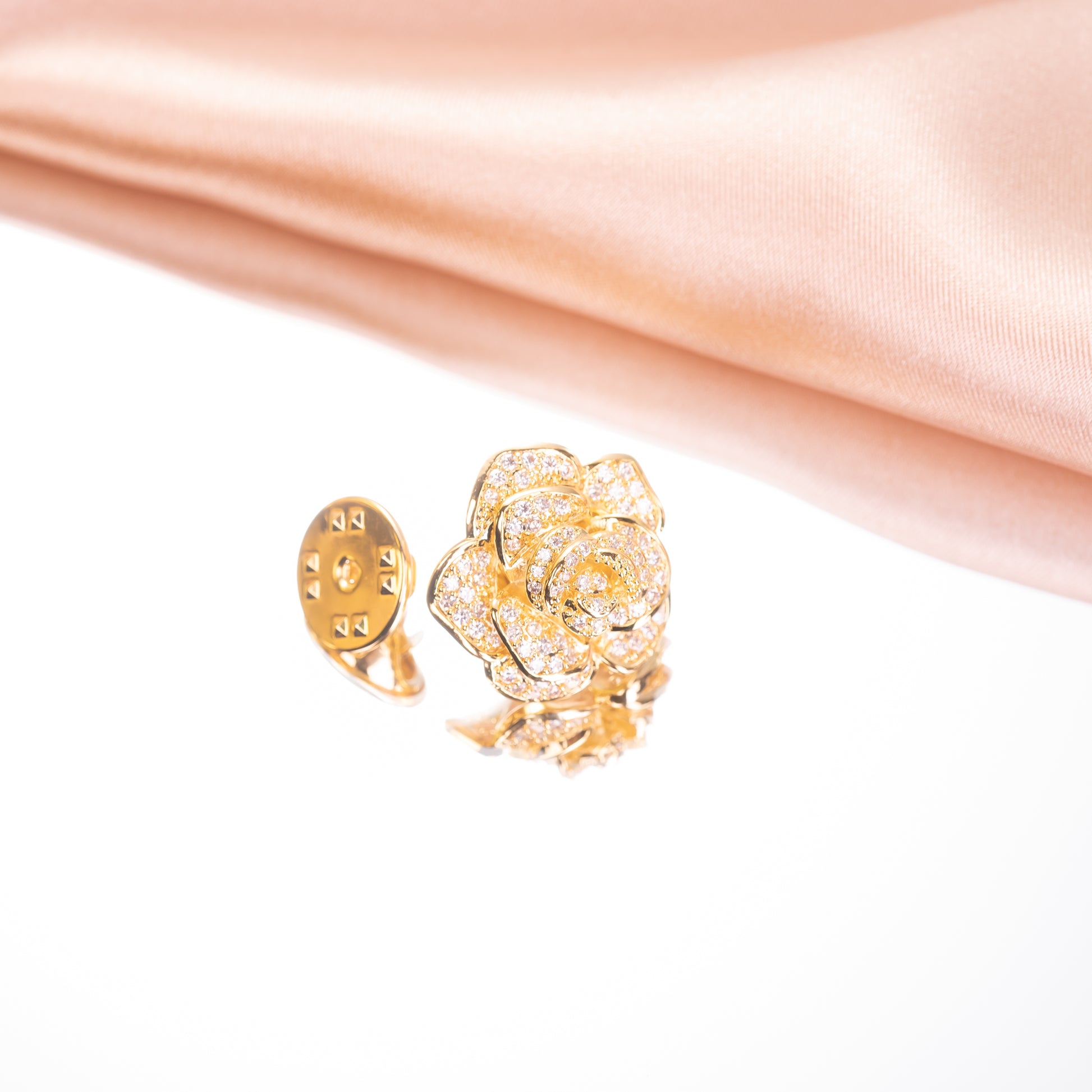 Gold ring with rose design on a pink fabric background