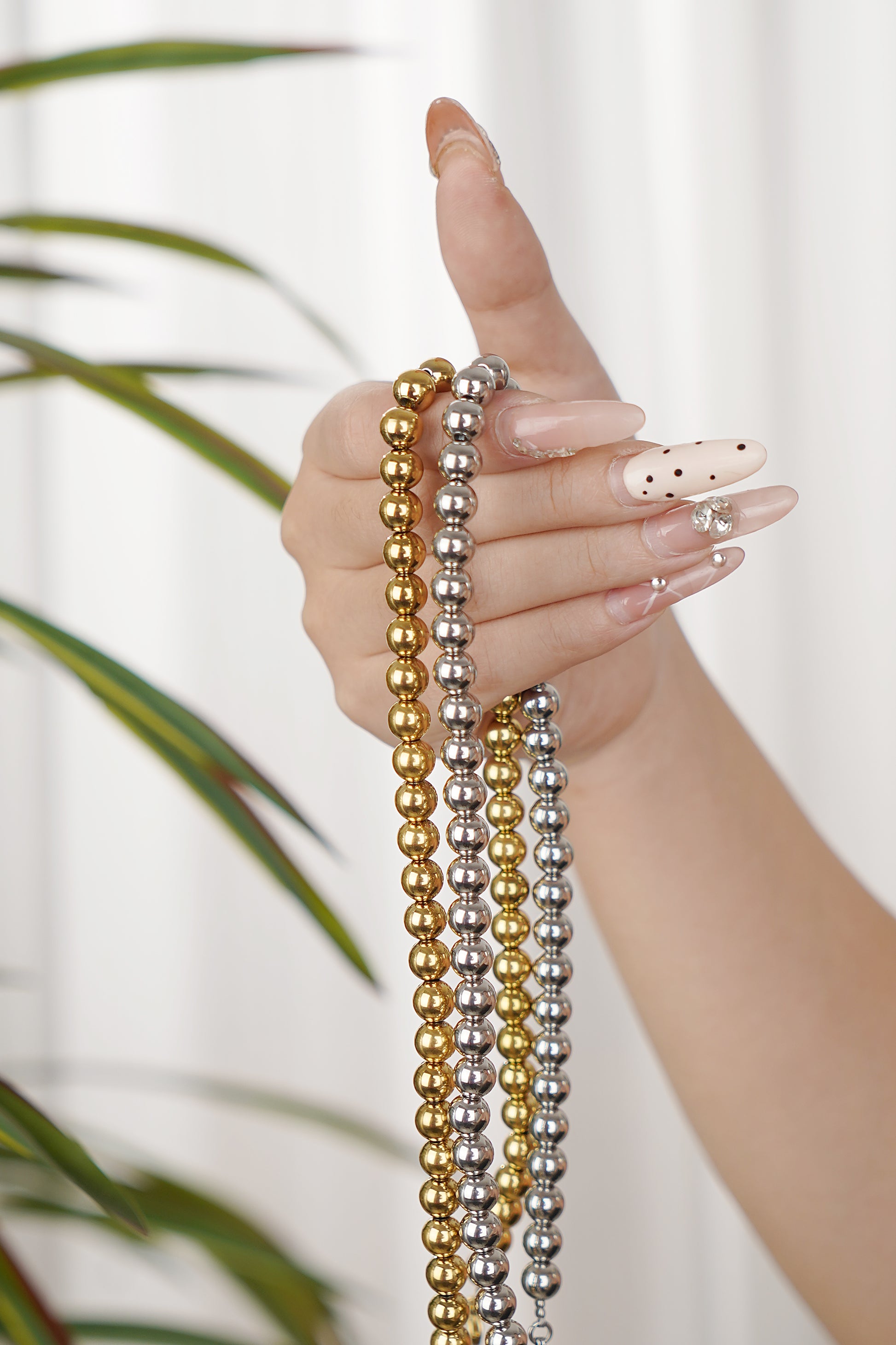 Hand holding three beaded Necklaces in gold, silver, and bronze against a blurred natural background