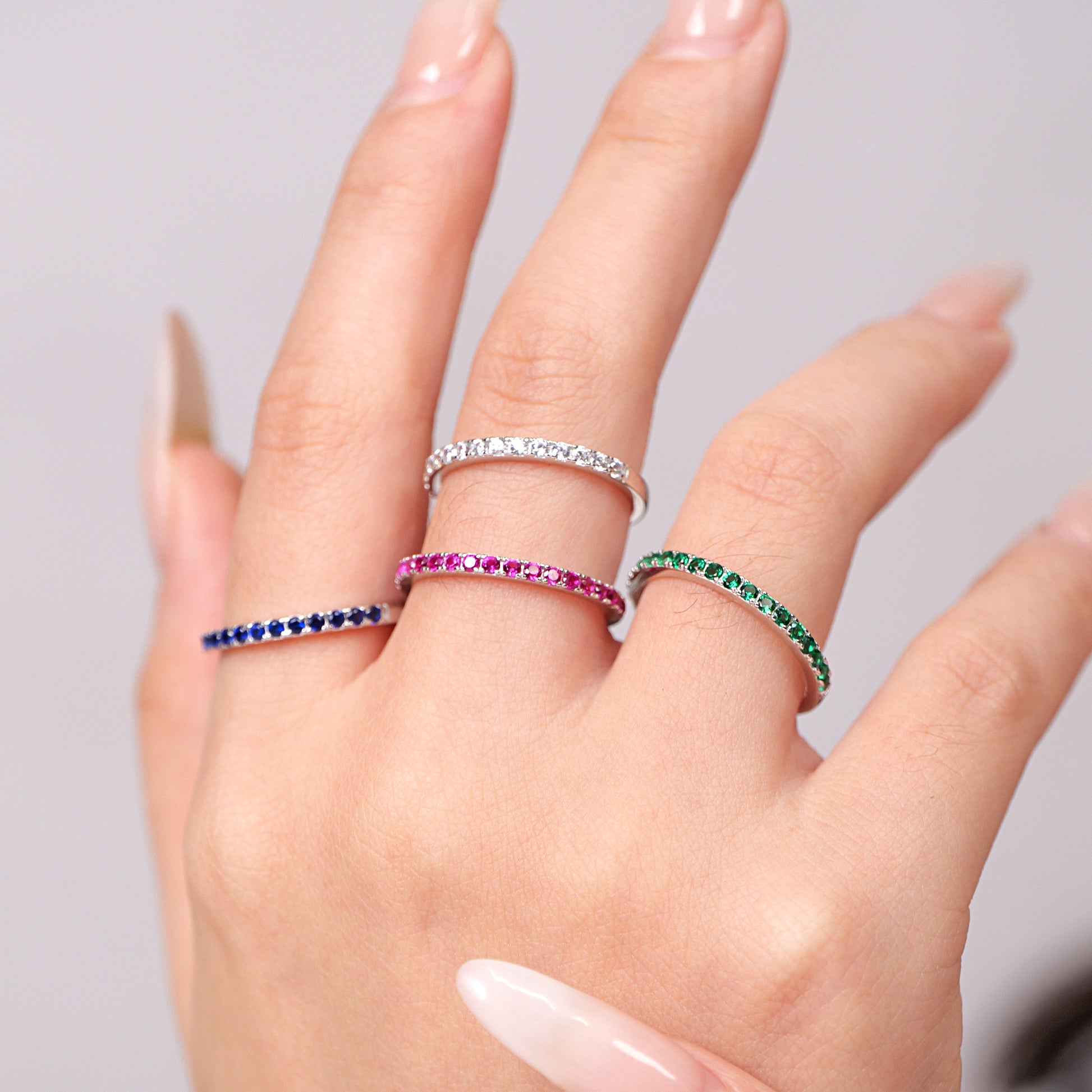 Hand wearing multiple rings with colored stones on a neutral background