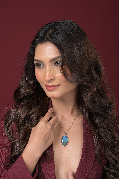 Woman wearing a necklace with a Labradorite pendant against a red background