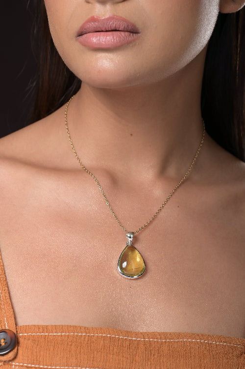 Close-up of a woman wearing a gold necklace with a teardrop-shaped amber pendant.