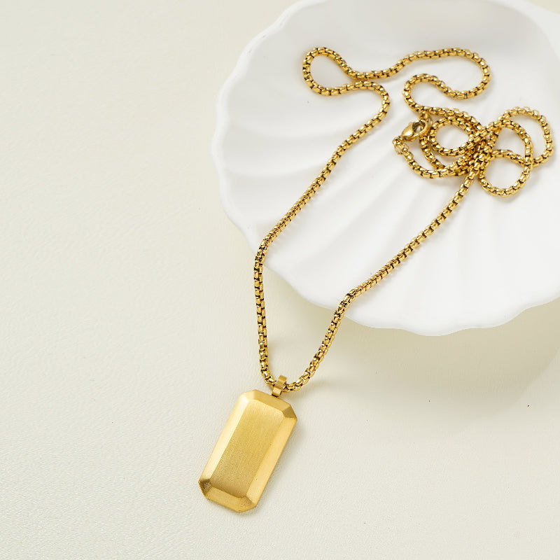 Gold necklace with a rectangular pendant on a white dish