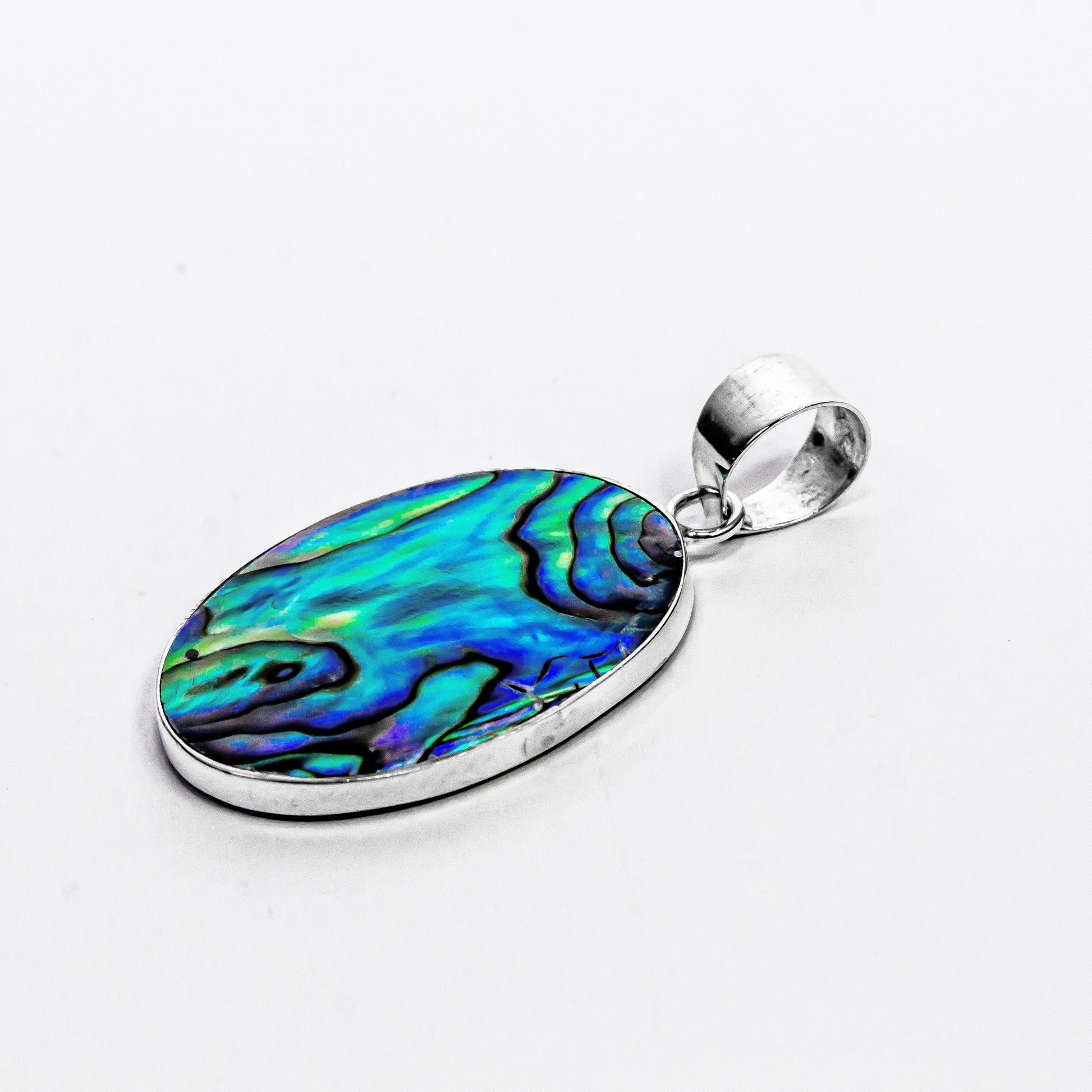 Oval abalone shell medallion pendant set in intricate sterling silver Balinese filigree design on white background