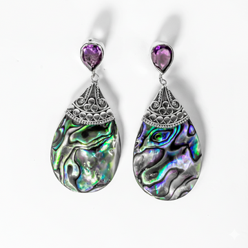 Pair of teardrop-shaped earrings with abalone shell design and purple gemstones on a white background.