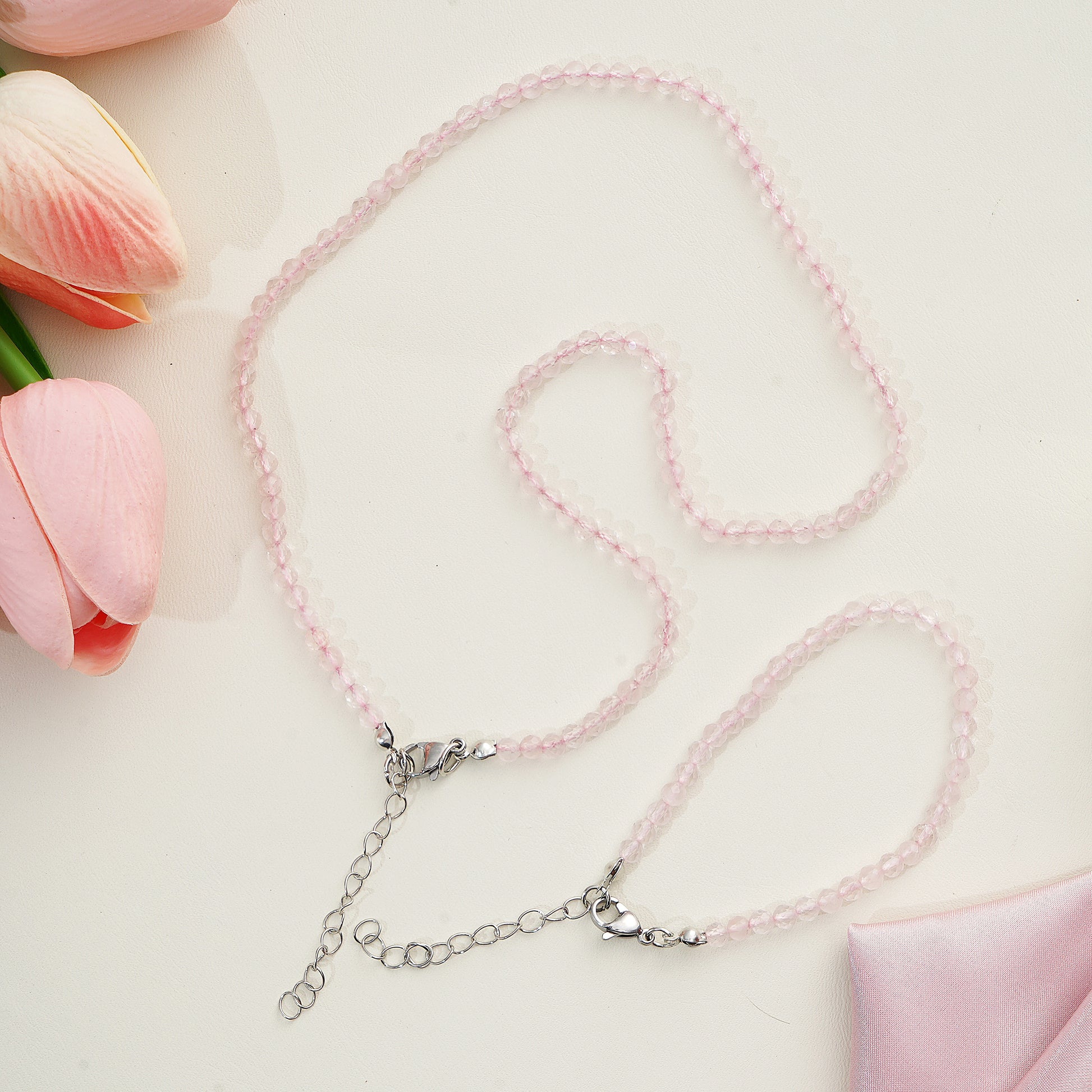 Pink beaded necklace with silver clasp on a light pink background with tulips